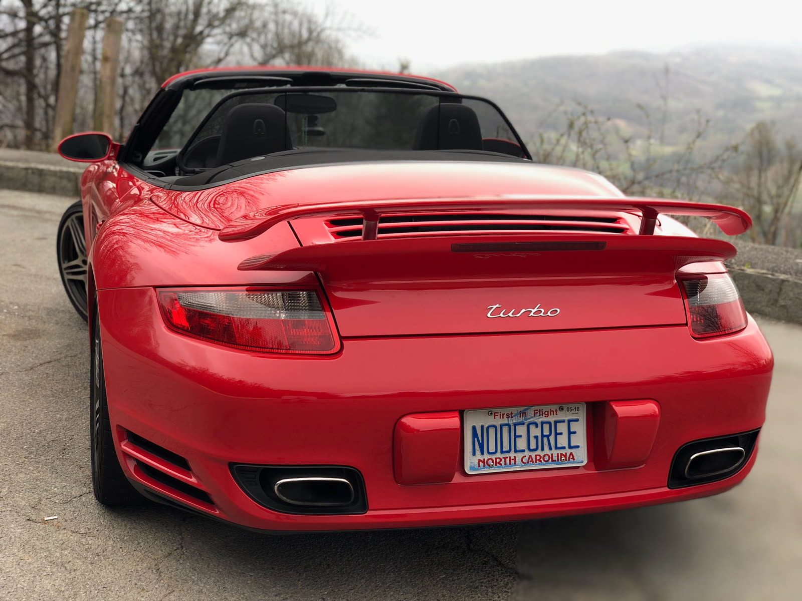 Rear of a red Porsche 911 Turbo cabriolet with a North Carolina NODEGREE plate, mountains behind