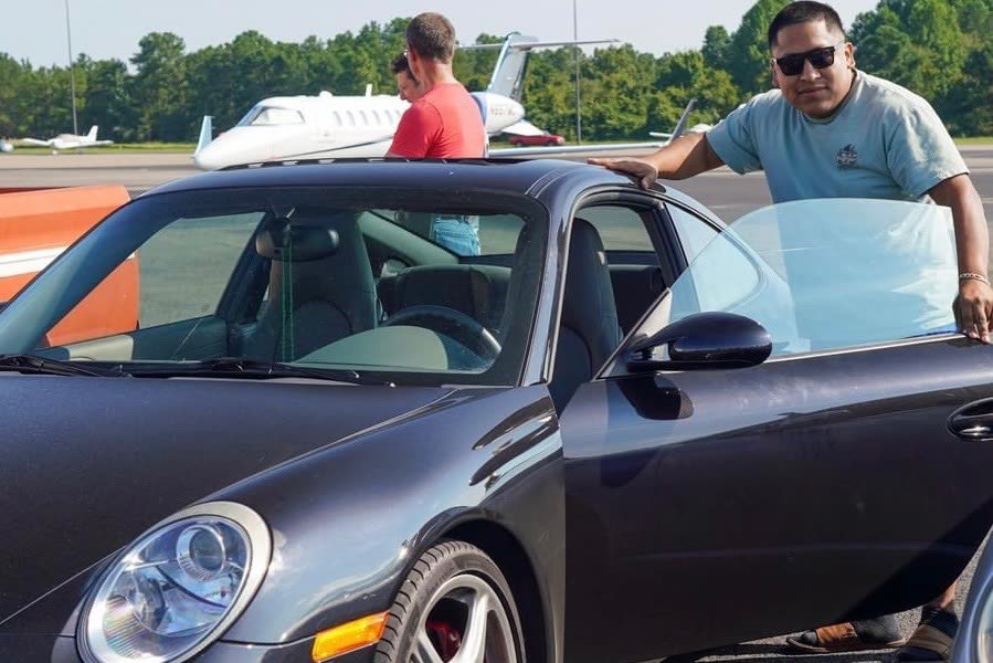 Saúl and a friend standing in the open doors of a dark Porsche 911 on an airfield