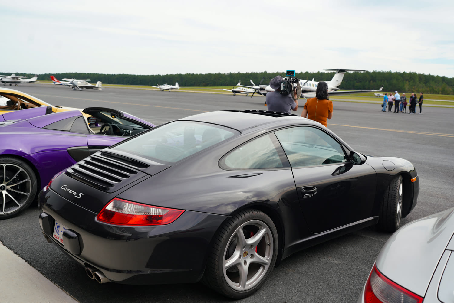 Black Porsche 911 parked in a row of sports cars at an airfield show