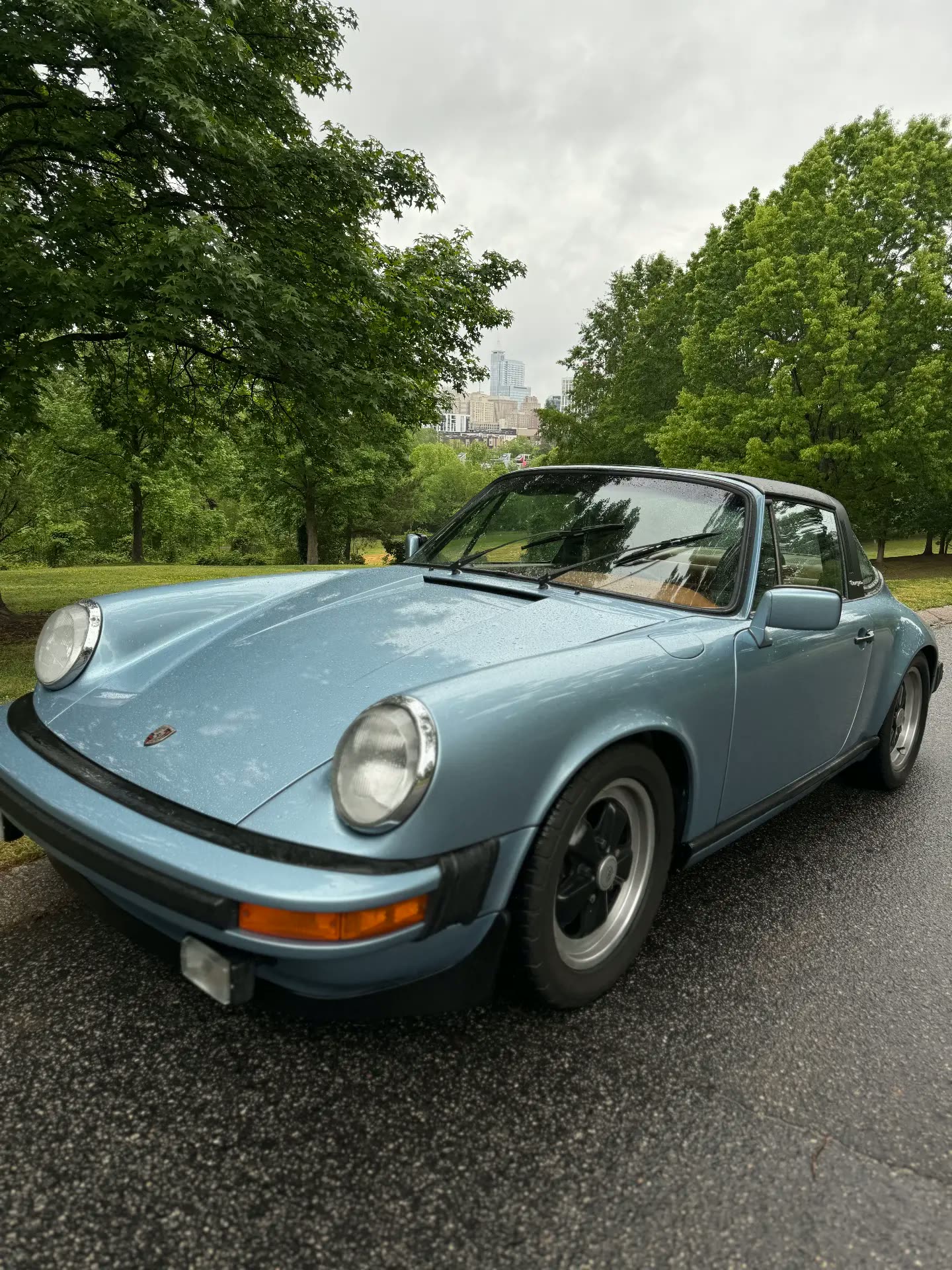 Light blue air-cooled Porsche 911 Targa parked on a tree-lined street