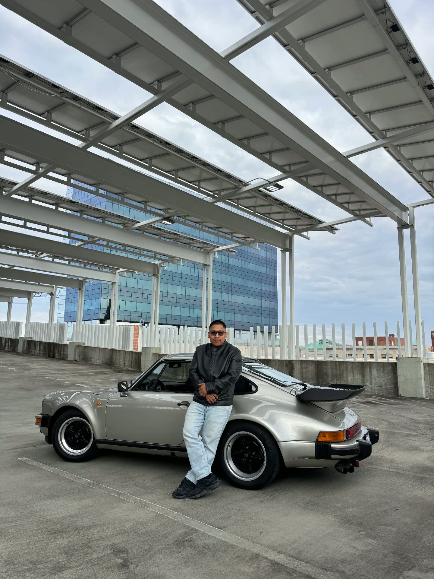 Saúl leaning against his silver air-cooled Porsche 911 Turbo in a parking deck